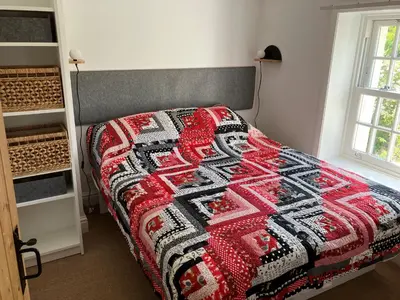 a bedroom with a red and black quilt on a bed at 2a Coastguard Cottages in Gorran Haven