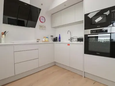 a white kitchen with white cabinets and a clock on the wall at 5 Longshore in Newquay