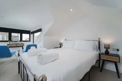 a bedroom with a large white bed and blue chairs at Burrow Cottage in St Ives