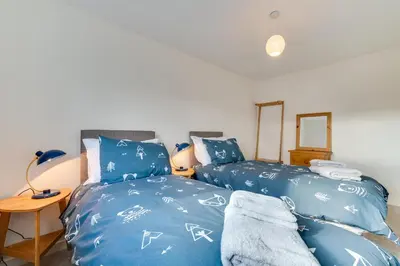 a bedroom with two beds with blue sheets and a table at 2 Bed in St. Eval oc-boaths in Saint Ervan