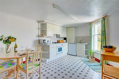a kitchen with white cabinets and a table and chairs at 1 Bed in Fowey oc-cmoonr in Fowey