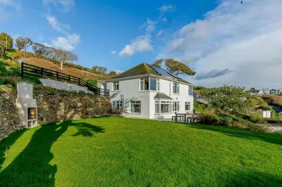 a white house with a stone wall and green grass at 4 Bed in Mawgan Porth oc-d26830 in Mawgan Porth