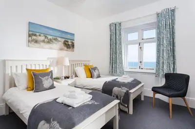 a bedroom with two beds and a chair and a window at Brook Cottage Cornwall in St Merryn