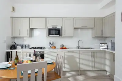 a kitchen with white cabinets and a wooden table at Brook Cottage Cornwall in St Merryn