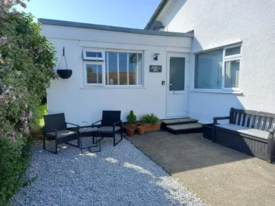 a patio with two chairs and a bench in front of a house at Ruby's Den in Carbis Bay