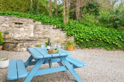 a picnic table with a bottle of wine and a bowl of fruit at 3 Bed in Little Petherick oc-maplod in Little Petherick