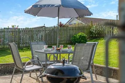 a table and chairs with a grill and an umbrella at 3 Bed in Padstow oc-p00131 in St Merryn