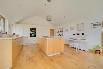 a large kitchen with white cabinets and a wooden floor at 3 Bed in Padstow oc-p00357 in St Merryn