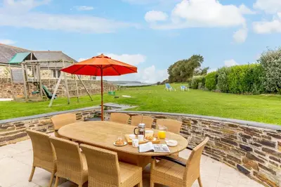 a wooden table with chairs and an umbrella on a patio at 3 Bed in Wadebridge oc-p00421 in Saint Issey