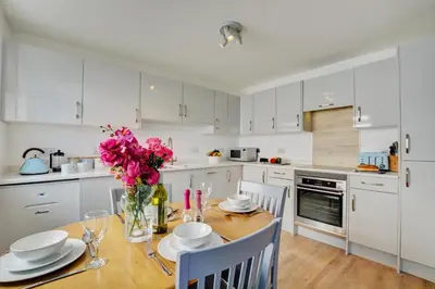 a kitchen with white cabinets and a wooden table with pink flowers at 2 Bed in Crackington Haven oc-p00596 in Crackington Haven