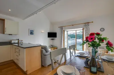 a kitchen and living room with a table with a vase of flowers at 2 Bed in Porthleven oc-quaysi in Porthleven