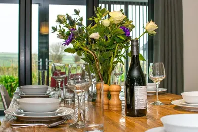 a table with a bottle of wine and a vase of flowers at 3 Bed in Trevone oc-stcad in Padstow