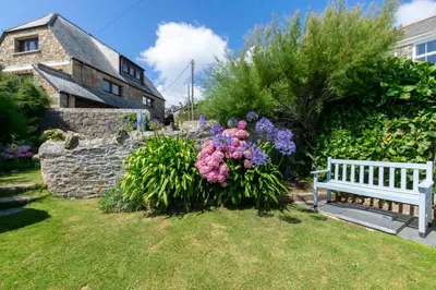 a bench in a yard with flowers and a stone wall at 2 Bed in Porthleven oc-stmich in Porthleven
