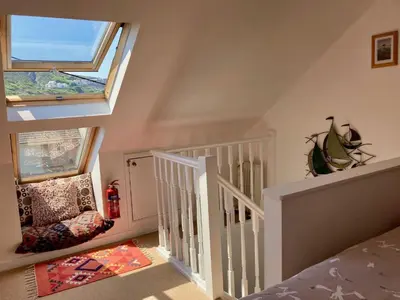 a white staircase with two windows and a chair at 'Anchor Point', Porthtowan in Porthtowan