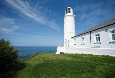 a lighthouse on top of a hill next to a building at Nimbus Cottage in St Merryn