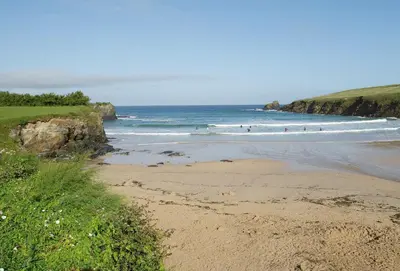 a beach with people surfing in the ocean at Owl House in Wadebridge