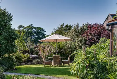 a table and chairs with an umbrella in a garden at Tregadjack Farmhouse in Crowan