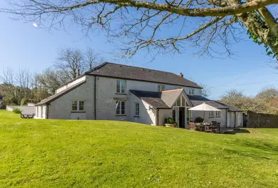 a large white house on a grassy hill at Bonython Farmhouse in Helston