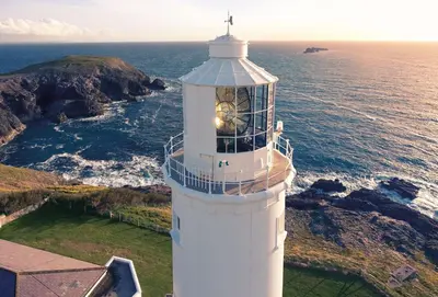 a lighthouse with a clock on it next to the ocean at Pelorus Cottage in St Merryn