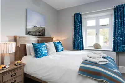 a bedroom with a large bed with blue curtains at Pelorus Cottage in St Merryn