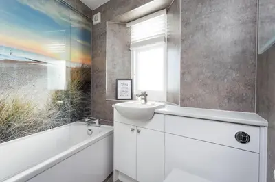 a white bathroom with a sink and a tub and a window at Pelorus Cottage in St Merryn