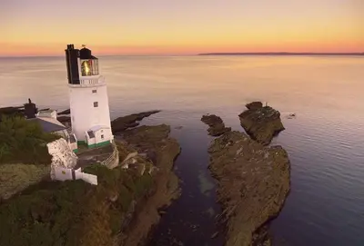 a lighthouse on a cliff in the water at sunset at Sally Port Cottage in Saint Mawes