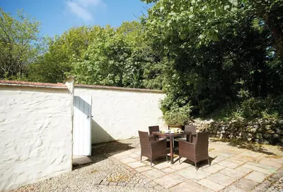a patio with a table and chairs next to a wall at Spring Water Barn in Helston