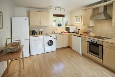 a large kitchen with white appliances and wooden floors at Mews Cottage in Helston