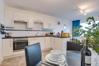 a kitchen with white cabinets and a table with a bottle of wine at 1 Bed in St Ives oc-cwn31 in St Ives