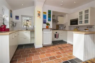 a kitchen with white cabinets and a red tile floor at Hideaway Tremayne in St Ives