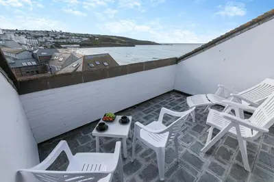 a balcony with white chairs and tables and the ocean at 2 Bed in St Ives oc-nic24 in St Ives