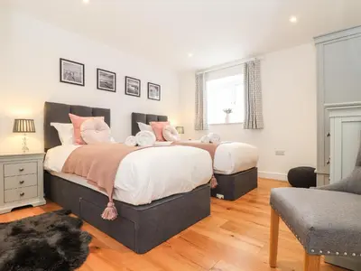 a bedroom with two beds and a chair at Trevilges Cottage in Helston