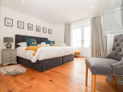 a bedroom with a large bed and a chair at Trevilges Cottage in Helston