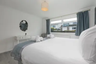 a white bedroom with a large bed and a window at Ocean Air in Carbis Bay