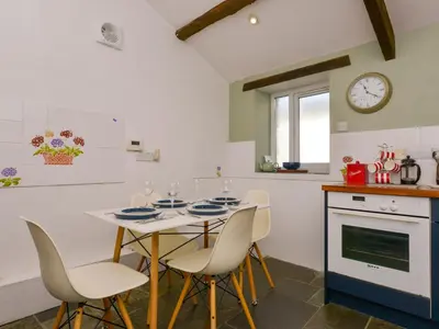 a kitchen with a table and chairs and a clock at Great Brightor Cob Barn in Bodmin