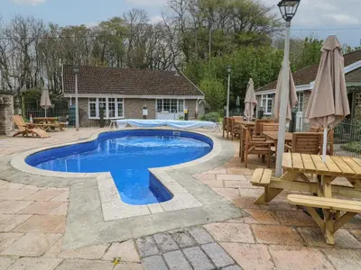 a swimming pool in a patio with a table and benches at Badger Sett in Granite Henge near Looe in Looe