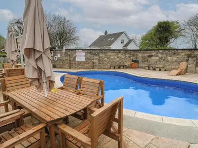 a wooden table and chairs next to a swimming pool at Badger Sett in Granite Henge near Looe in Looe