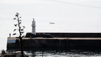 a lighthouse with a car parked next to the water at HipNautic, Mevagissey, Sleeps 6 in Mevagissey