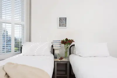 two beds in a bedroom with a table with flowers at Mordros, St Ives in St Ives