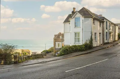 a white house on a street next to the ocean at Mordros, St Ives in St Ives