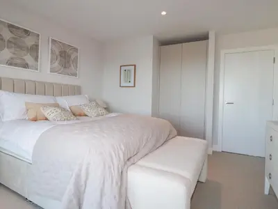 a white bedroom with a white bed and a bench at 7 Longshore in Newquay