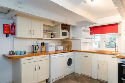a kitchen with white cabinets and a washer and dryer at St Samson in Port Isaac