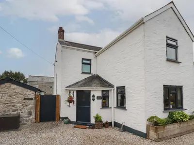 a white cottage with a black door and windows at Miners cottage in St Austell