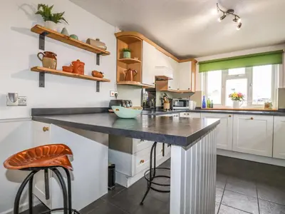 a kitchen with white cabinets and a counter with stools at Miners cottage in St Austell