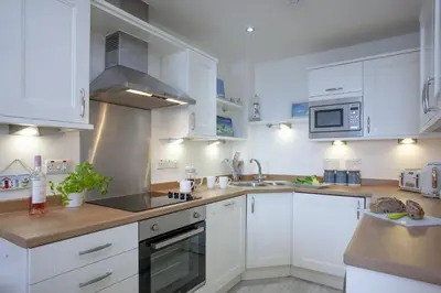 a kitchen with white cabinets and a sink at Fistral View, Pentire - Parking, Sea view, free Wifi in Newquay
