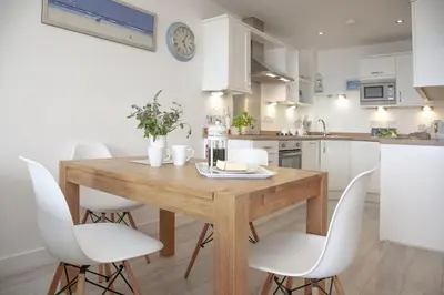 a kitchen with a wooden table and white chairs at Fistral View, Pentire - Parking, Sea view, free Wifi in Newquay