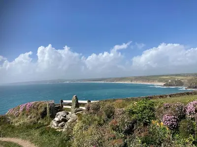 a bench on a hill next to the ocean at Olive's Cabin in Helston
