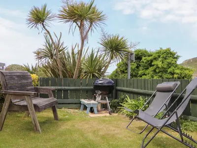 a grill and chairs in a backyard with palm trees at Kingsholm in Truro