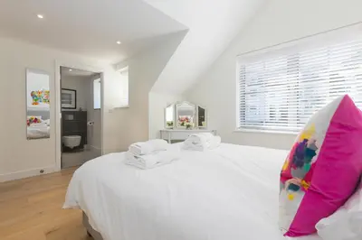 a white bedroom with a large white bed with a pink pillow at Bay View in St Ives