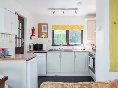 a kitchen with white cabinets and a sink and a window at Cross Cottage in Saint Breward